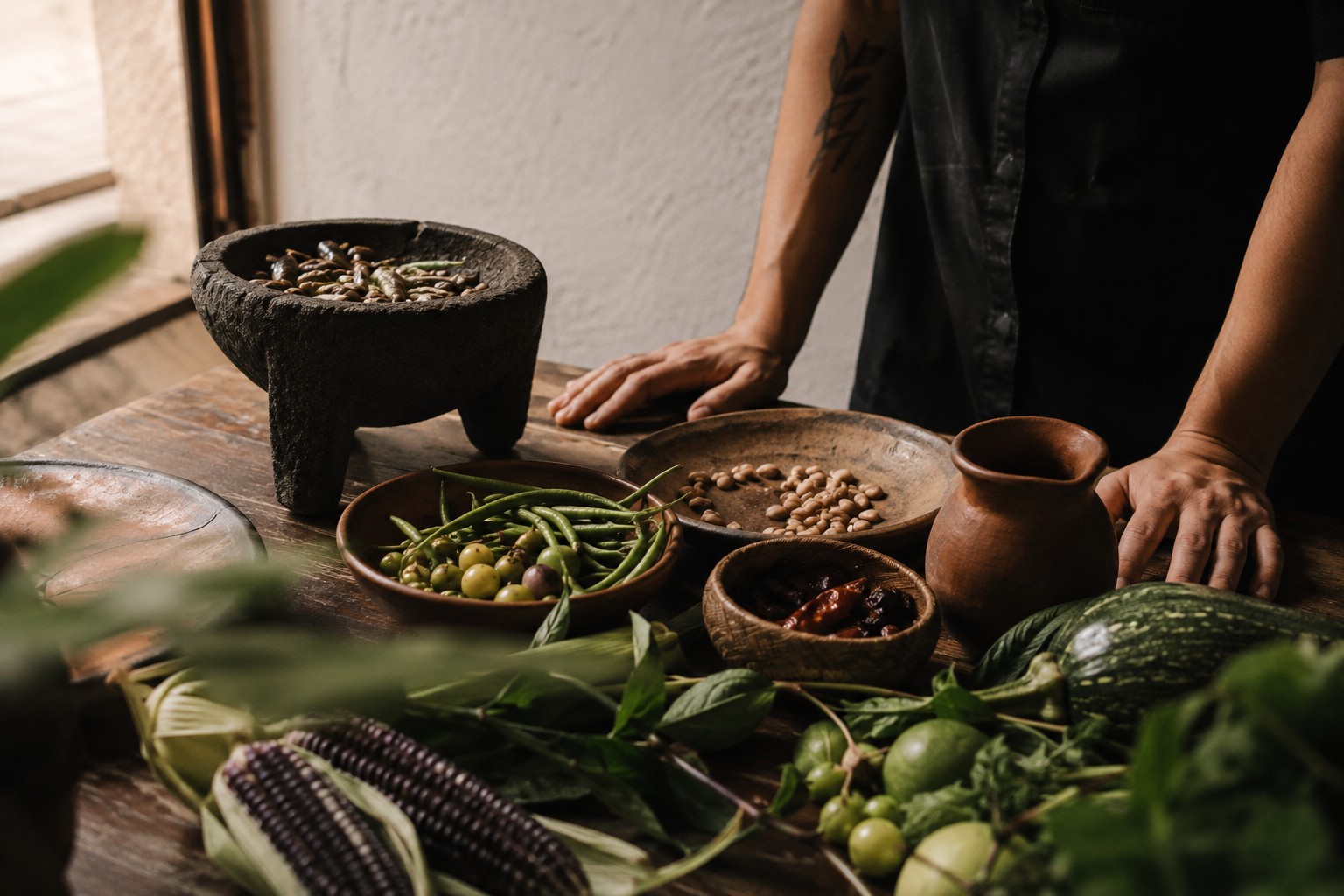 Ingredientes de temporada, utensilios de barro y manos de cocinero sobre una mesa de trabajo en Surqué.
